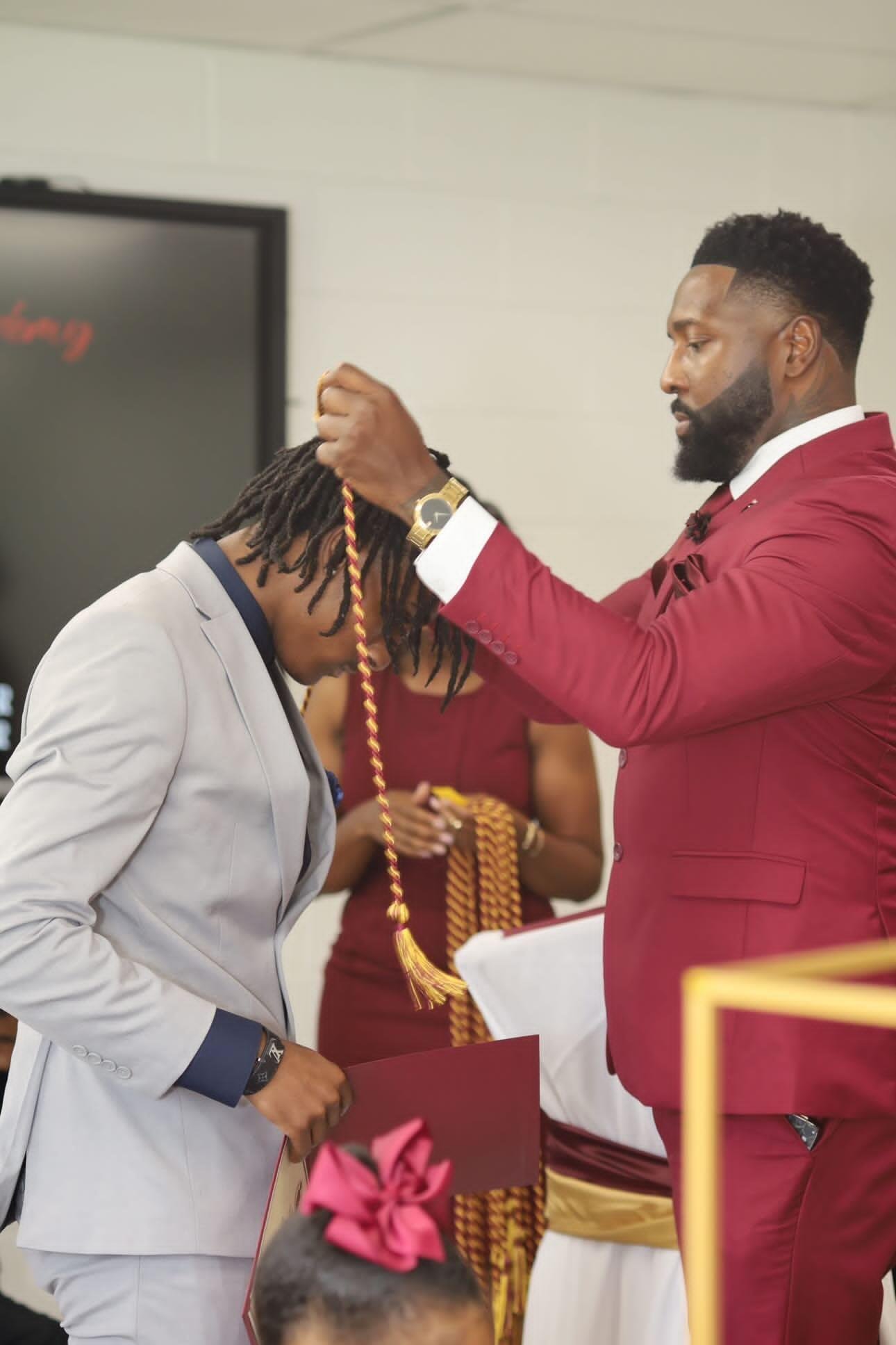 Close-up photo of Houston Owens cording a graduating student in a gray suit during the Krowwn Barber Academy ceremony.
