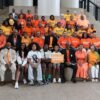 Large group photo of community leaders, residents, youth, and advocates gathered on the steps inside Mobile Government Plaza during a Project Wear Orange event. Participants are dressed primarily in orange shirts and clothing, many displaying messages supporting the effort to end gun violence. Several individuals wear NAACP apparel, while others hold signs promoting violence prevention and community safety. The diverse group poses together in a show of unity, solidarity, and commitment to raising awareness about gun violence and supporting safer communities in Mobile, Alabama.