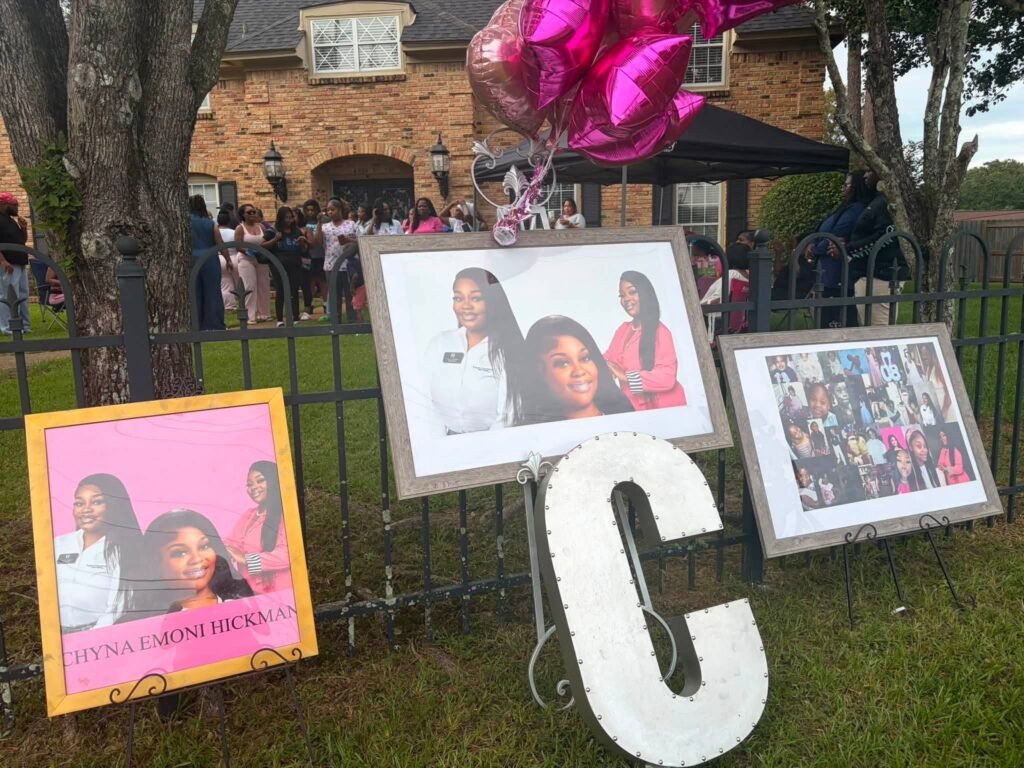 A memorial display set up on a lawn with framed photographs of Chyna Emoni Hickman, a large silver "C" letter, pink balloons, and community members gathered in the background.