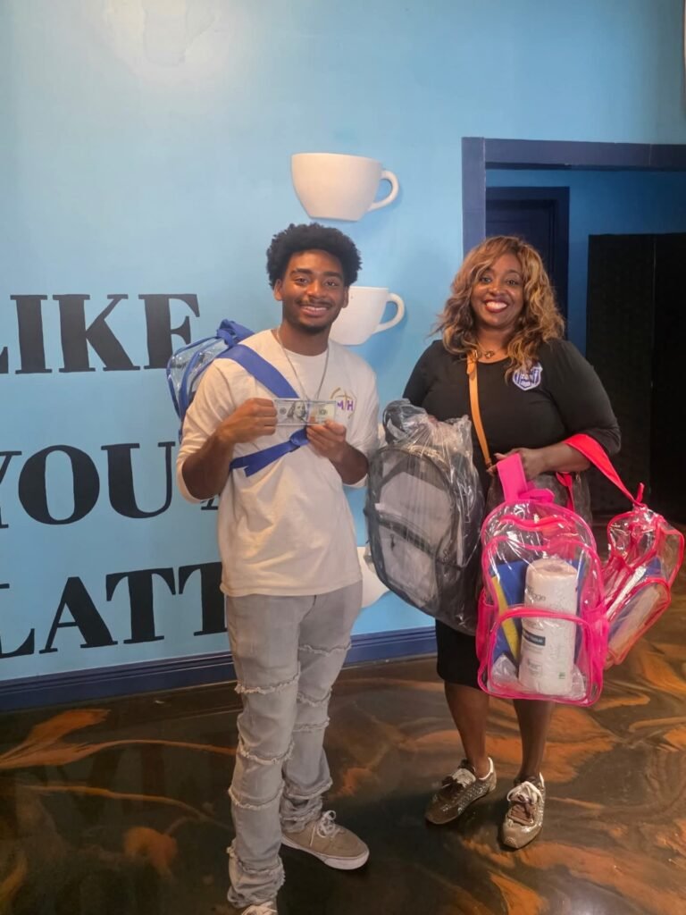 Kimberly Levingston, CEO of the Prichard Housing Authority, and a young man, holding clear backpacks, school supplies, and a donation inside Great Day Latte.