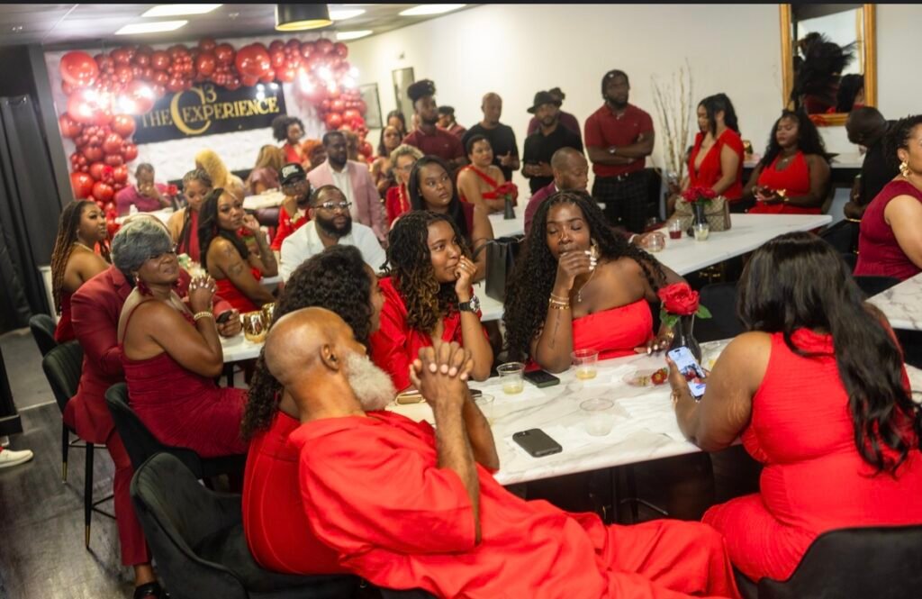 A crowded room of guests dressed in red and burgundy attire seated at tables and watching toward the front during the Rosé At Night event at the C3 Experience.