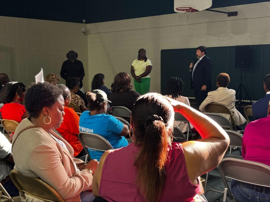 Community members seated in folding chairs listening to Smith and Mobile Mayor Spiro Cheriogotis answering their questions and addressing concerns at the Africatown Welcome Center information meeting.
