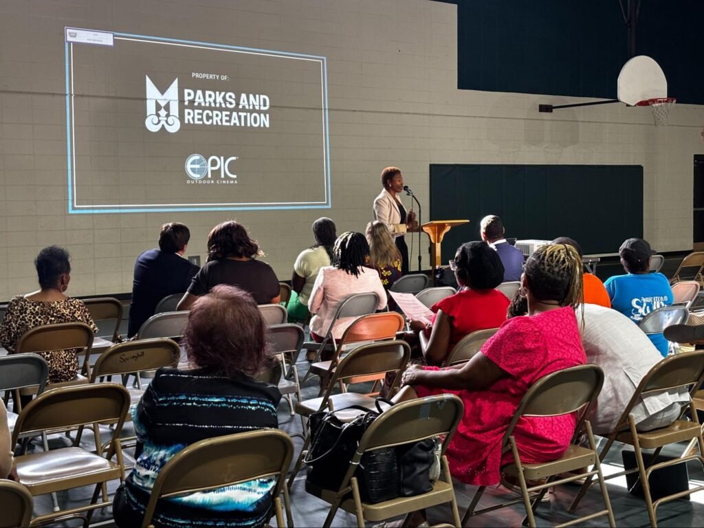Community members seated in folding chairs listening to District 2 Councilwoman Samantah Ingram opened the meeting holding a microphone at the Africatown Welcome Center information meeting.