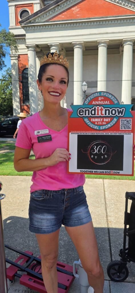 Felicia Marchetti wearing a crown and pink shirt, smiling while holding a colorful official sponsor sign featuring the "360 by FE" logo for the 8th annual endITnow Family Day at Cathedral Square.