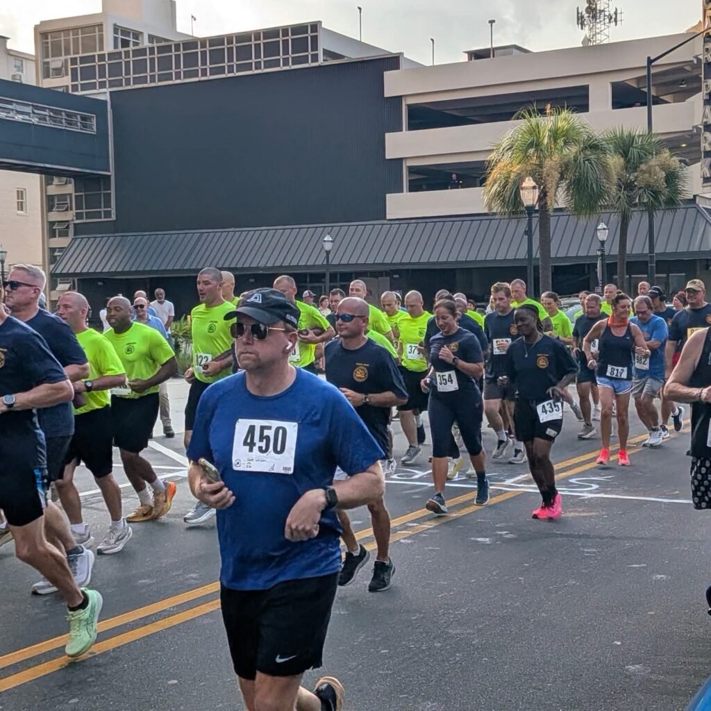 articipants wearing numbered race bibs jogging down a downtown Mobile street.
