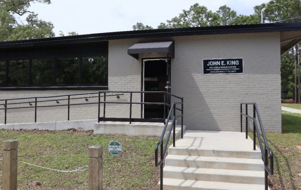 Exterior view of the John E. King Hillsdale Senior Center featuring light gray brick, a dark entrance awning, and handrails leading to the doorway.