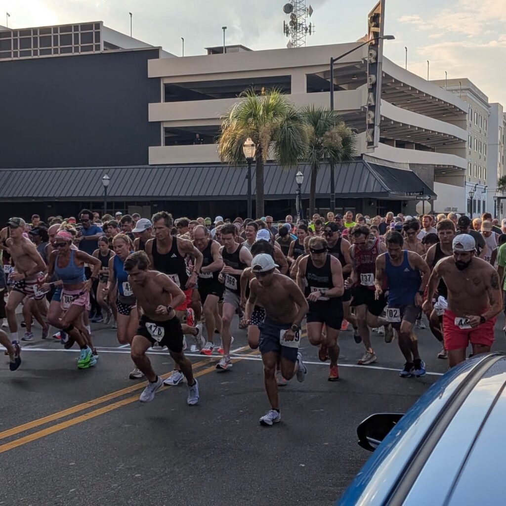 A large group of runners at the start line of a downtown Mobile 5K event.