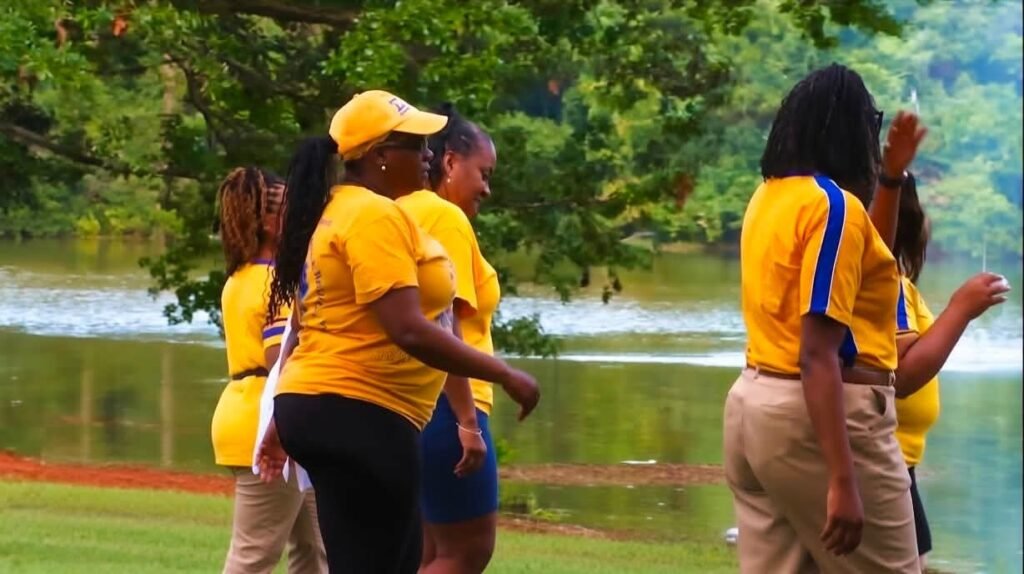 A group of people wearing yellow and blue apparel walking outdoors along a grassy slope near a body of water at Tricentennial Park.