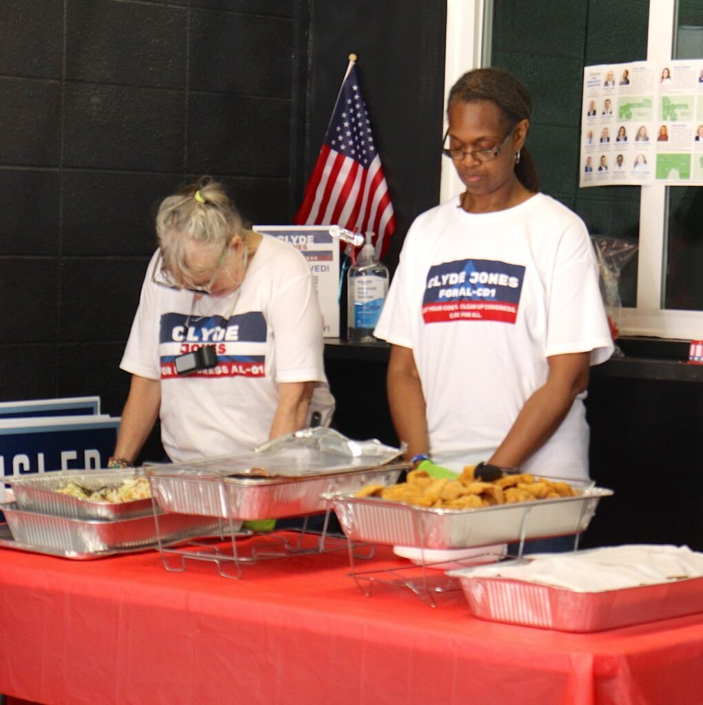 Two campaign representatives wearing white Clyde Jones for Congress t-shirts bow their heads during a prayer over the food at the Mobile headquarters grand opening event.