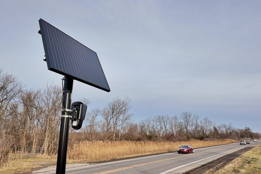Solar-powered automated license plate reader camera mounted on a roadside pole alongside a highway.