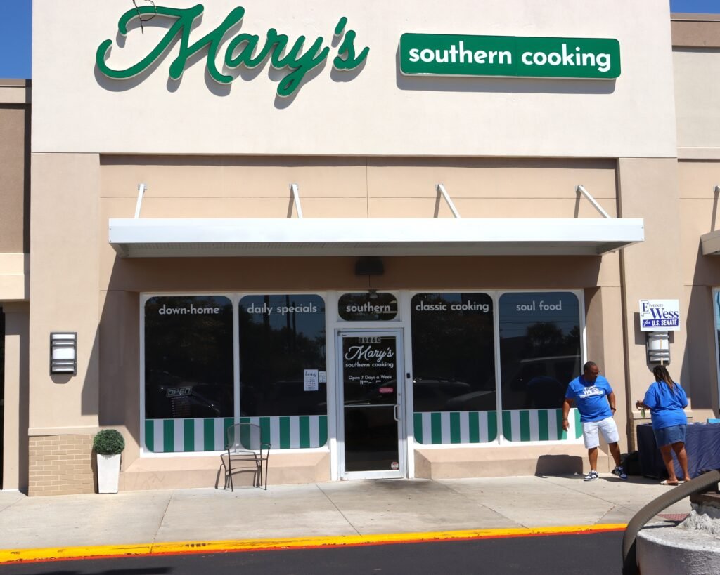 The storefront exterior of Mary's Southern Cooking restaurant featuring green and white signs and campaign volunteers by the entrance.