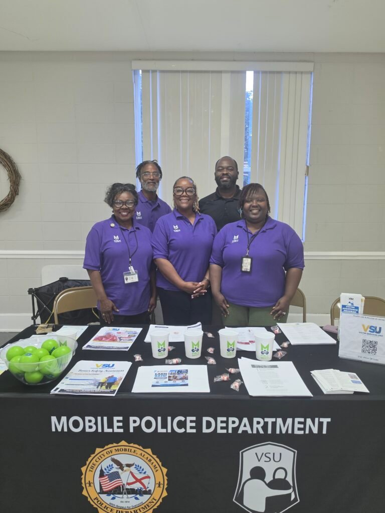 Five people wearing purple shirts stand behind a black table featuring the Mobile Police Department seal and VSU logo.