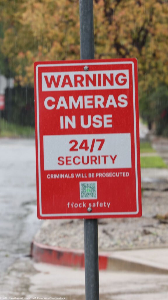 Red warning sign reading "Warning Cameras in Use 24/7 Security" featuring a Flock Safety QR code.