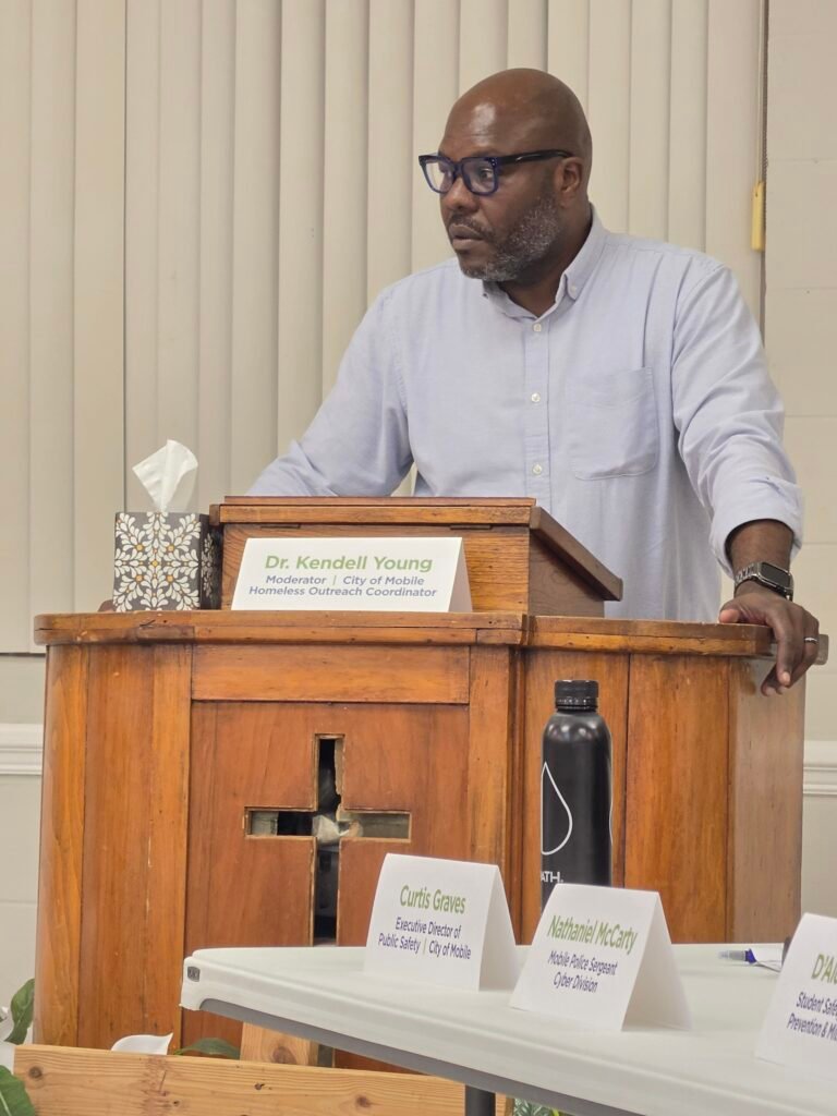 Dr. Kendall Young stands behind a wooden podium featuring his name and title card at the front of the room.