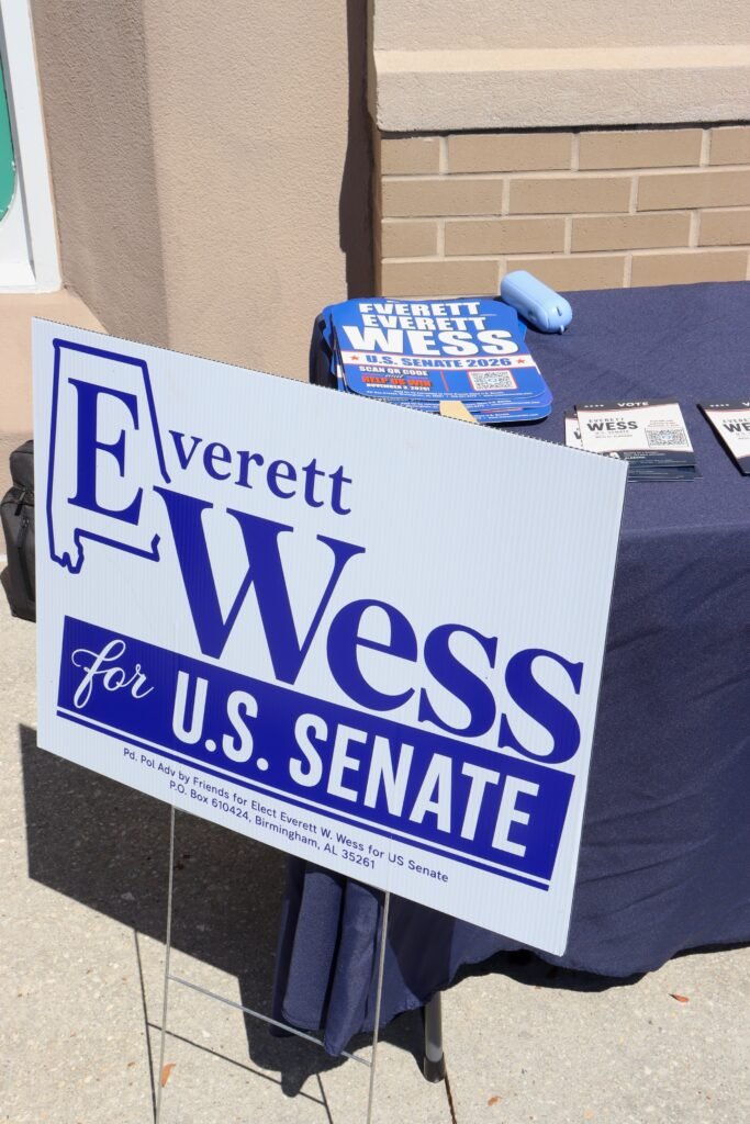 A white and blue Everett Wess for U.S. Senate campaign yard sign standing in front of a donation table.
