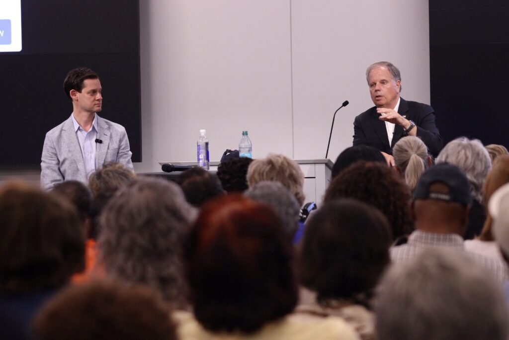 Phillip Ensler and Doug Jones seated on stage facing an audience at the Mobile town hall.
