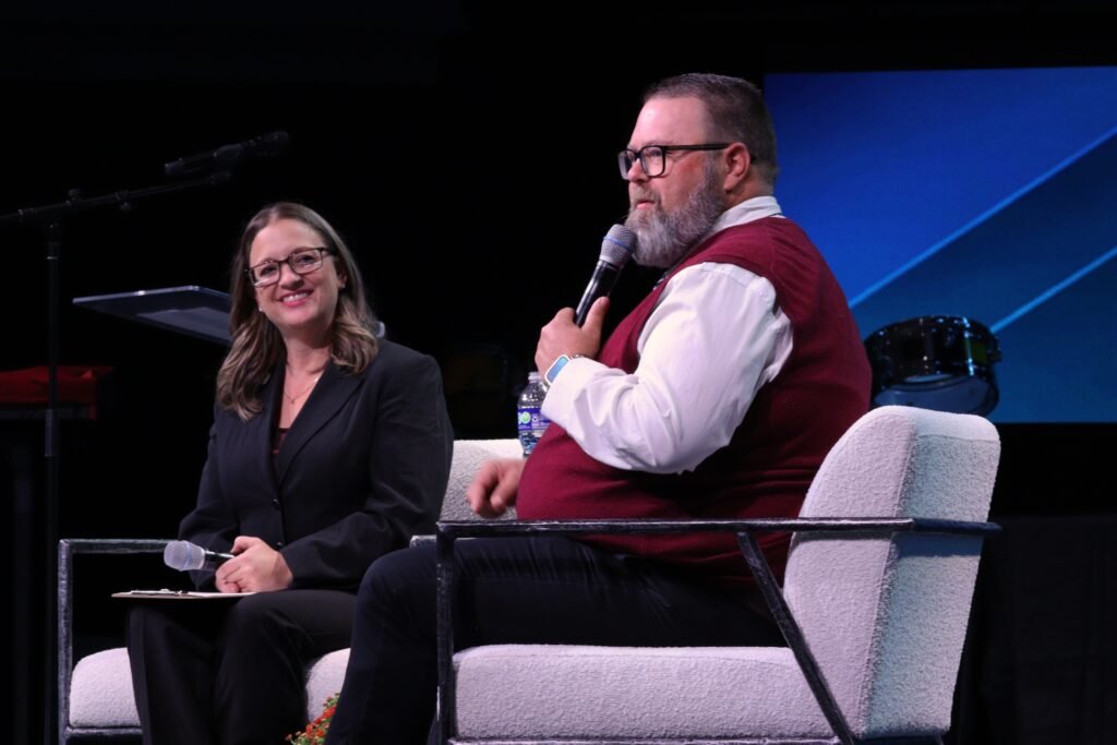 Mayor Brandon Van Hook sits in an armchair on stage holding a microphone and speaking