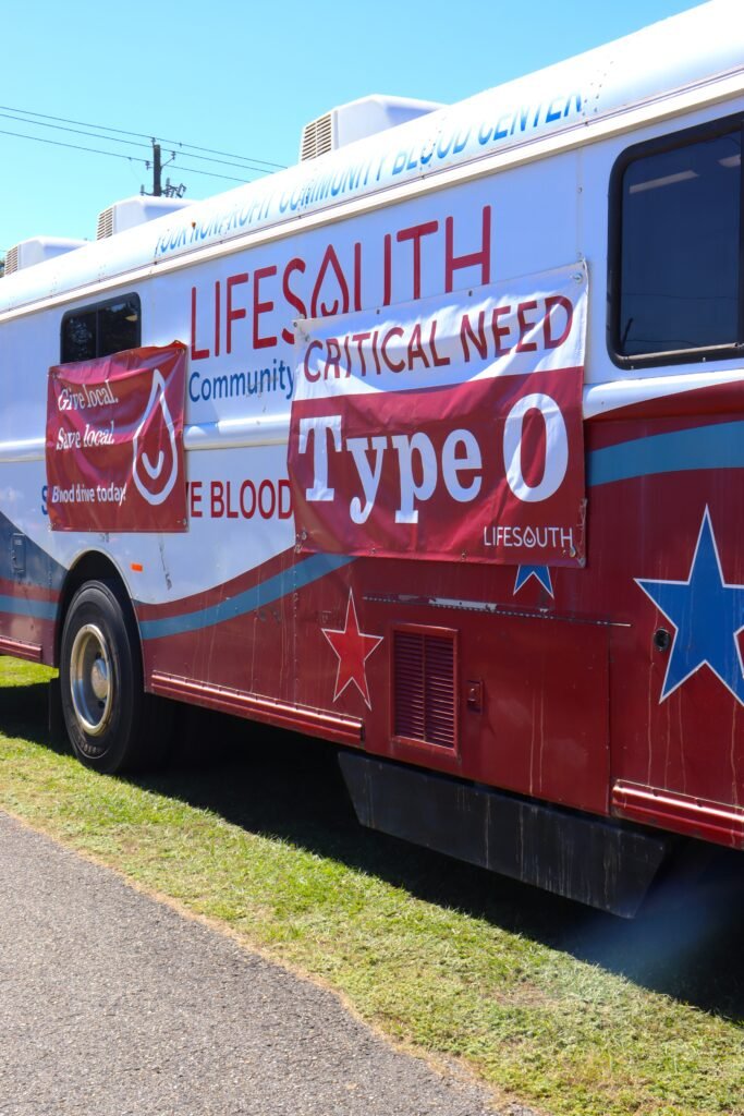 A white and red LifeSouth Community Blood Centers bloodmobile parked on grass with a banner highlighting a critical need for Type O blood.