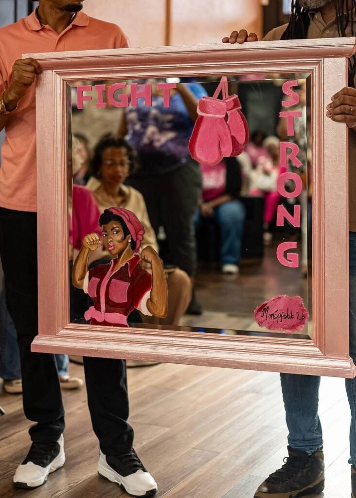 A rose-gold framed mirror held by two people, featuring painted designs of pink boxing gloves, a woman flexing her arm, and the words Fight and Strong.