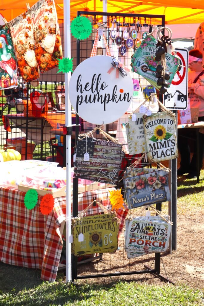 An outdoor vendor market stand displaying autumn-themed signs including one that reads "hello pumpkin" and another that says "Mimi's Place".