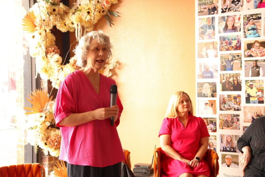 Breast cancer survivor Donna stands holding a microphone to share her recovery story at Great Day Latte during the Ma’am in the Mirror event.